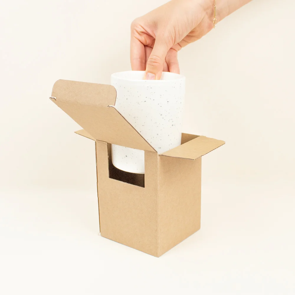 Mano sacando una taza de cerámica blanca de una caja de cartón
