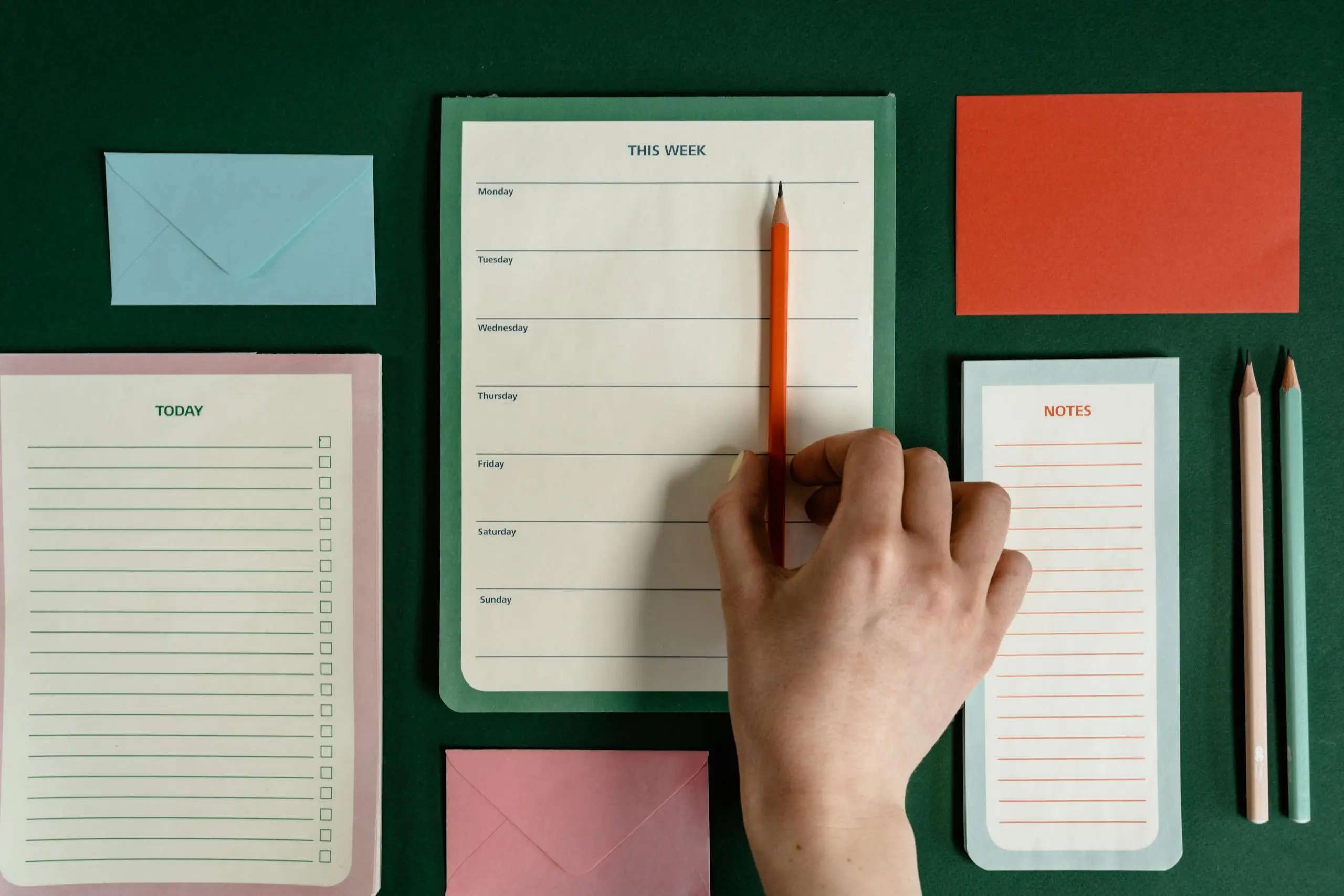 Imagen cenital de una mano colocando un lápiz sobre una mesa de trabajo con diferentes productos de papelería