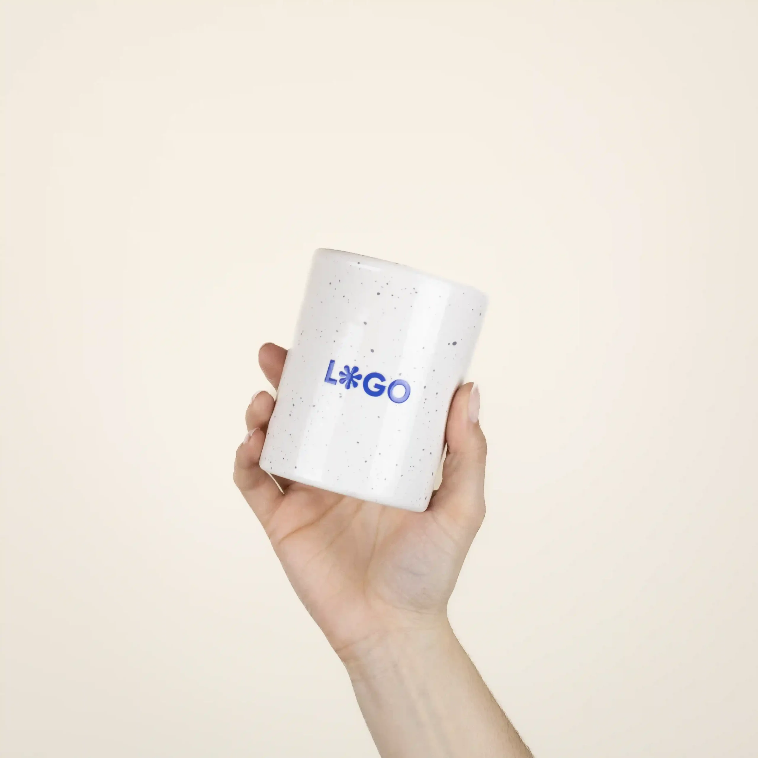 Mano mostrando una taza de cerámica blanca con puntos negros personalizada con la palabra logo en azul