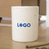 Taza de cerámica blanca con puntos negros personalizada con logo azul sobre una mesa de madera