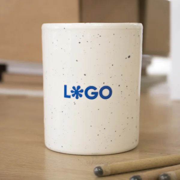 Taza de cerámica blanca con puntos negros personalizada con logo azul sobre una mesa de madera