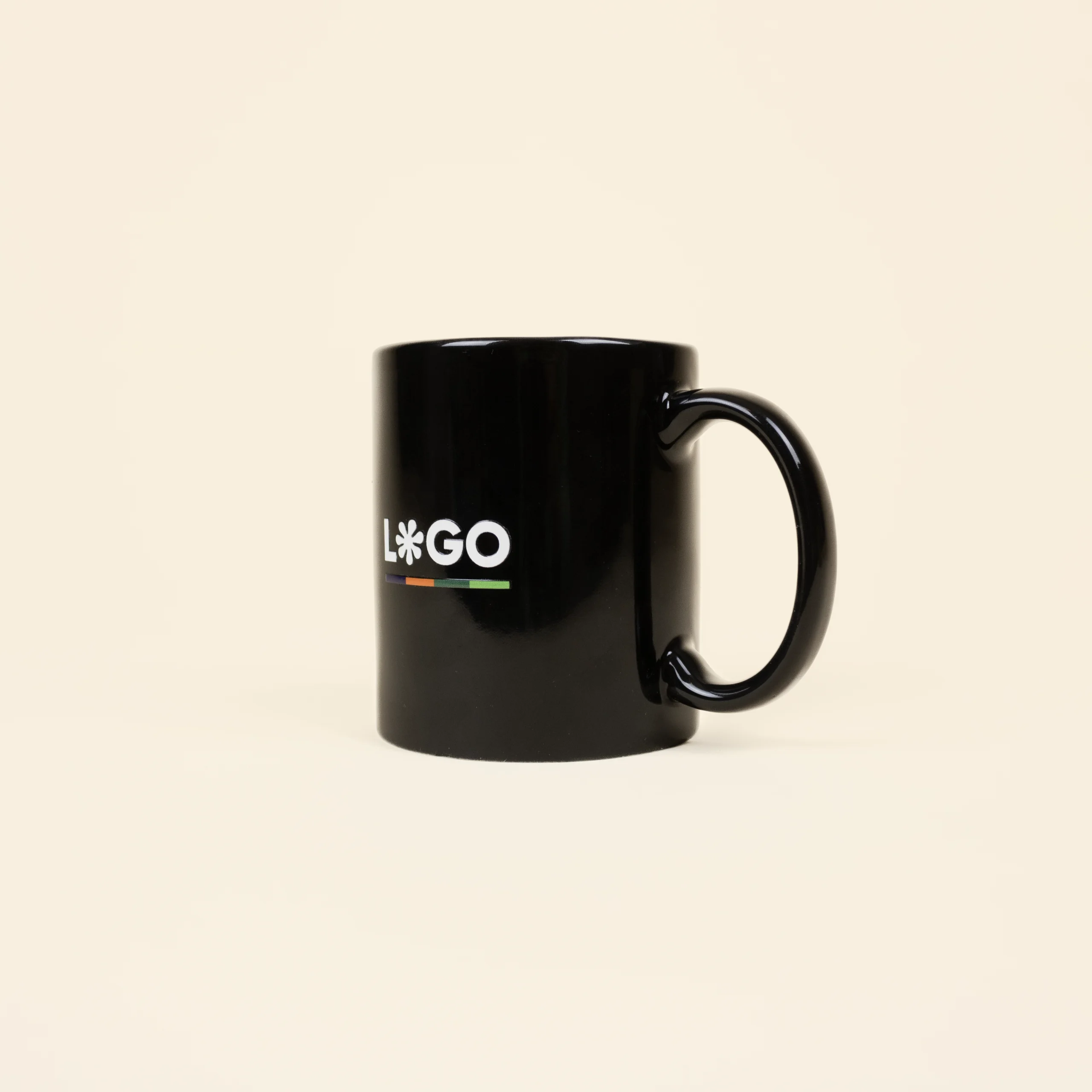 Taza negra con asa personalizada con la palabra logo en blanco fotografiada sobre un fondo beige
