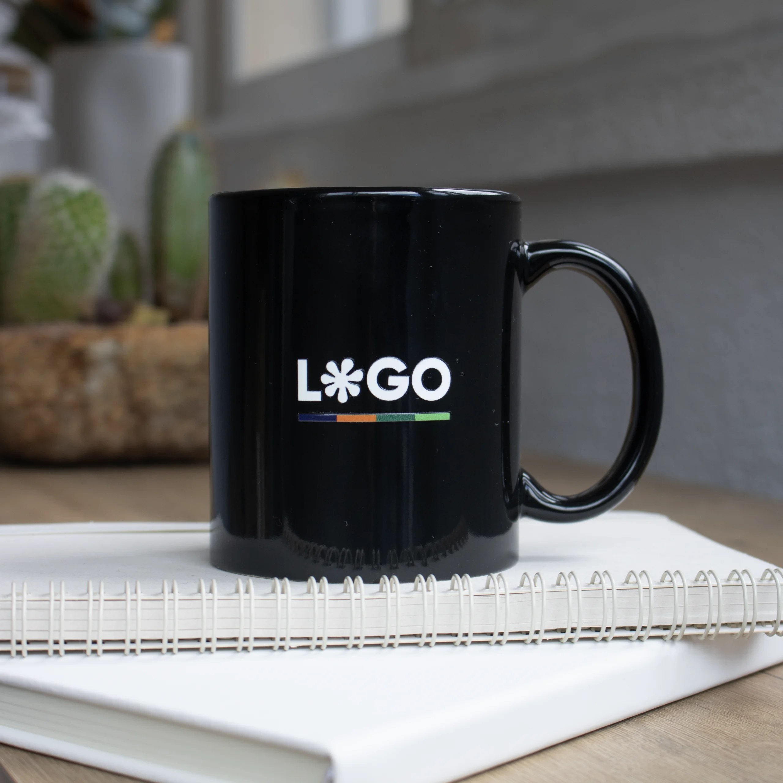 Taza negra con asa personalizada con la palabra logo en blanco colocada encima de un cuaderno blanco