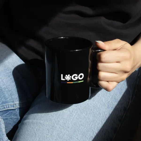 Chica en vaqueros agarrando una taza negra con asa personalizada con la palabra logo en blanco