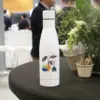 Botella blanca de acero inoxidable personalizada sobre una mesa en una sala de eventos