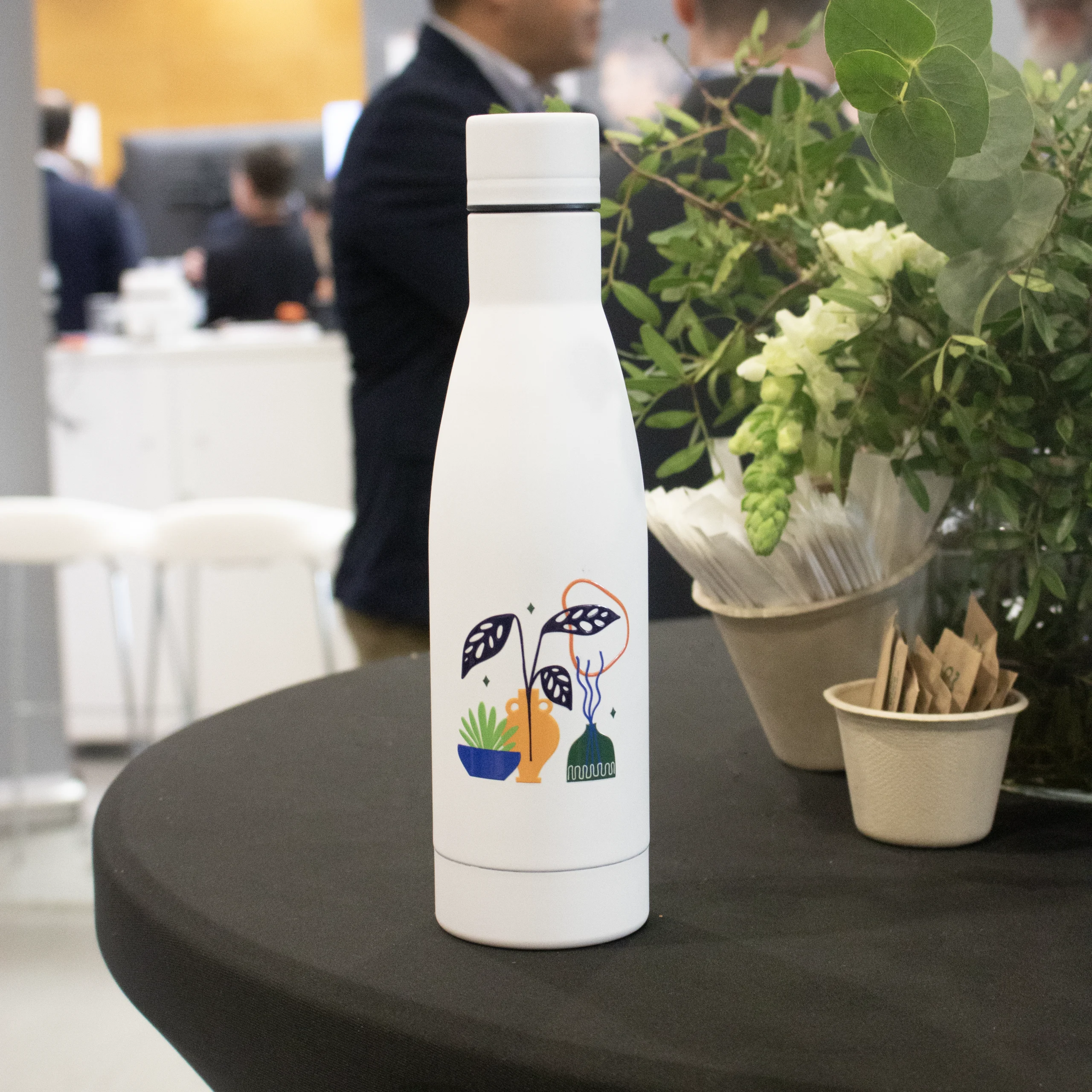 Botella blanca de acero inoxidable personalizada sobre una mesa en una sala de eventos