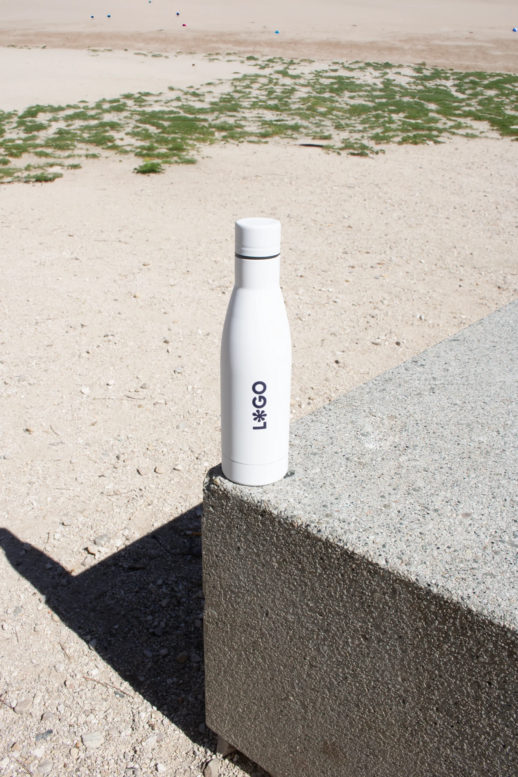 Botellas sostenibles personalizadas. Botella BALANCE. Botella blanca de acero inoxidable personalizada con logo azul apoyada en la calle