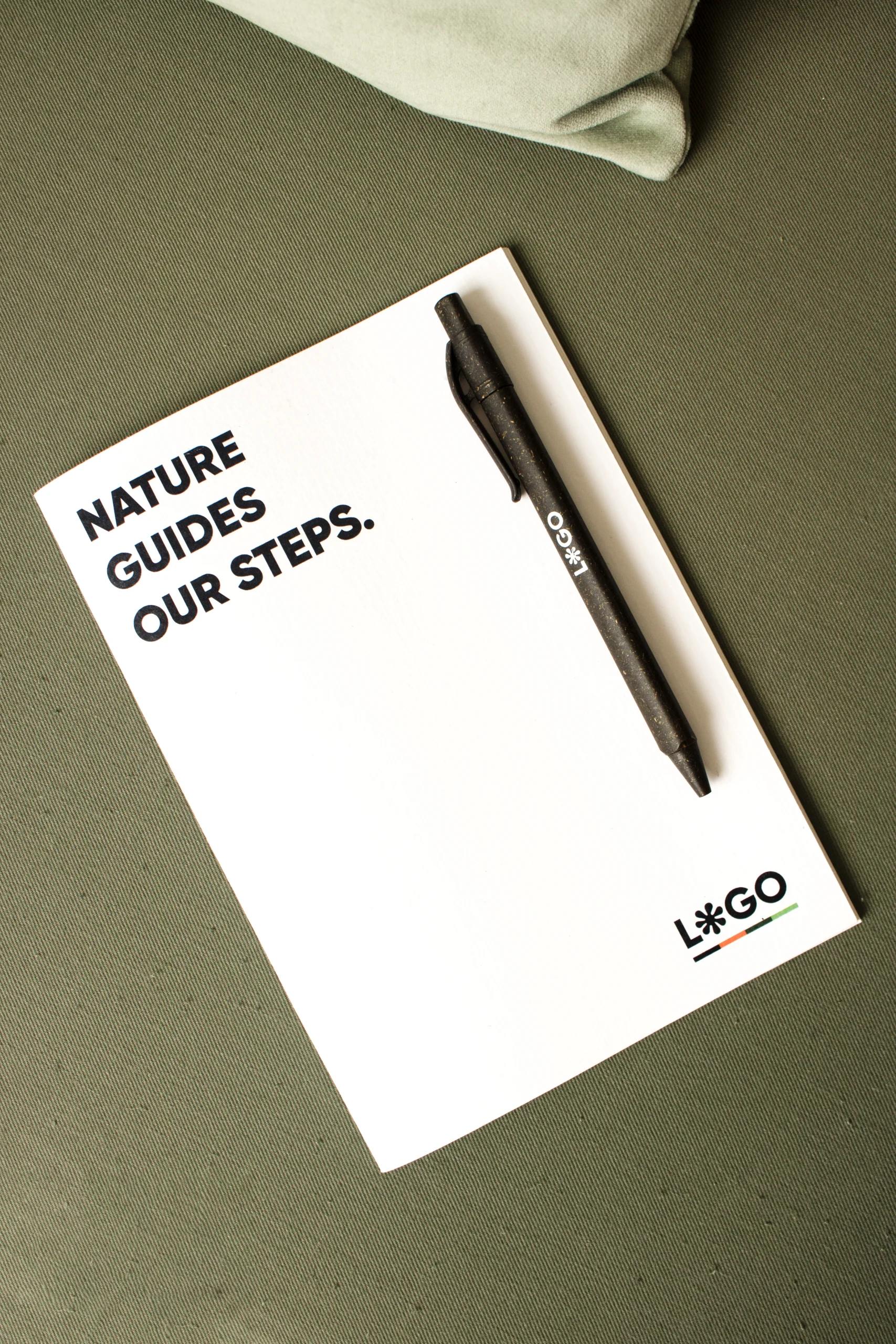Cuaderno de grapa ecológico blanco personalizado con bolígrafo marrón fondo verde