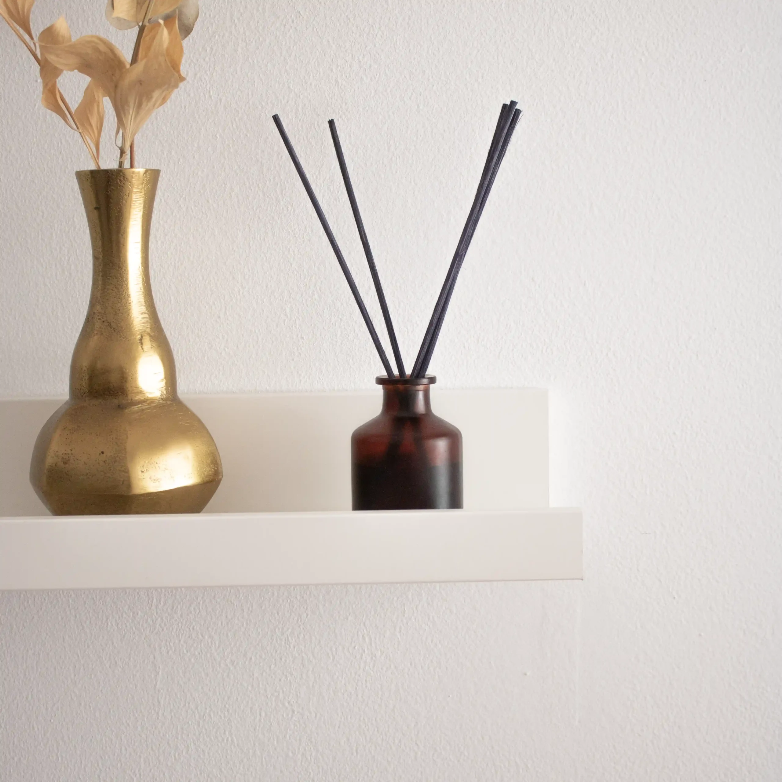 Diffuseur Mikado personnalisé en verre brun sur une étagère blanche