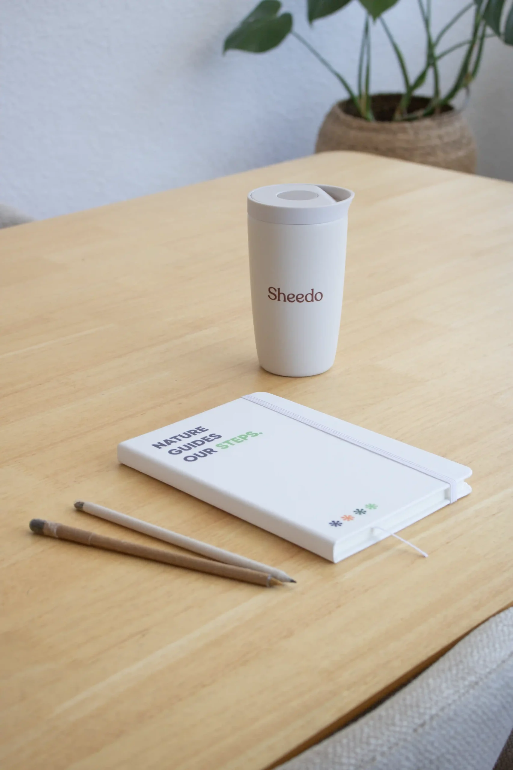 Mesa de madera con cuaderno reciclado blanco lápices y taza beige