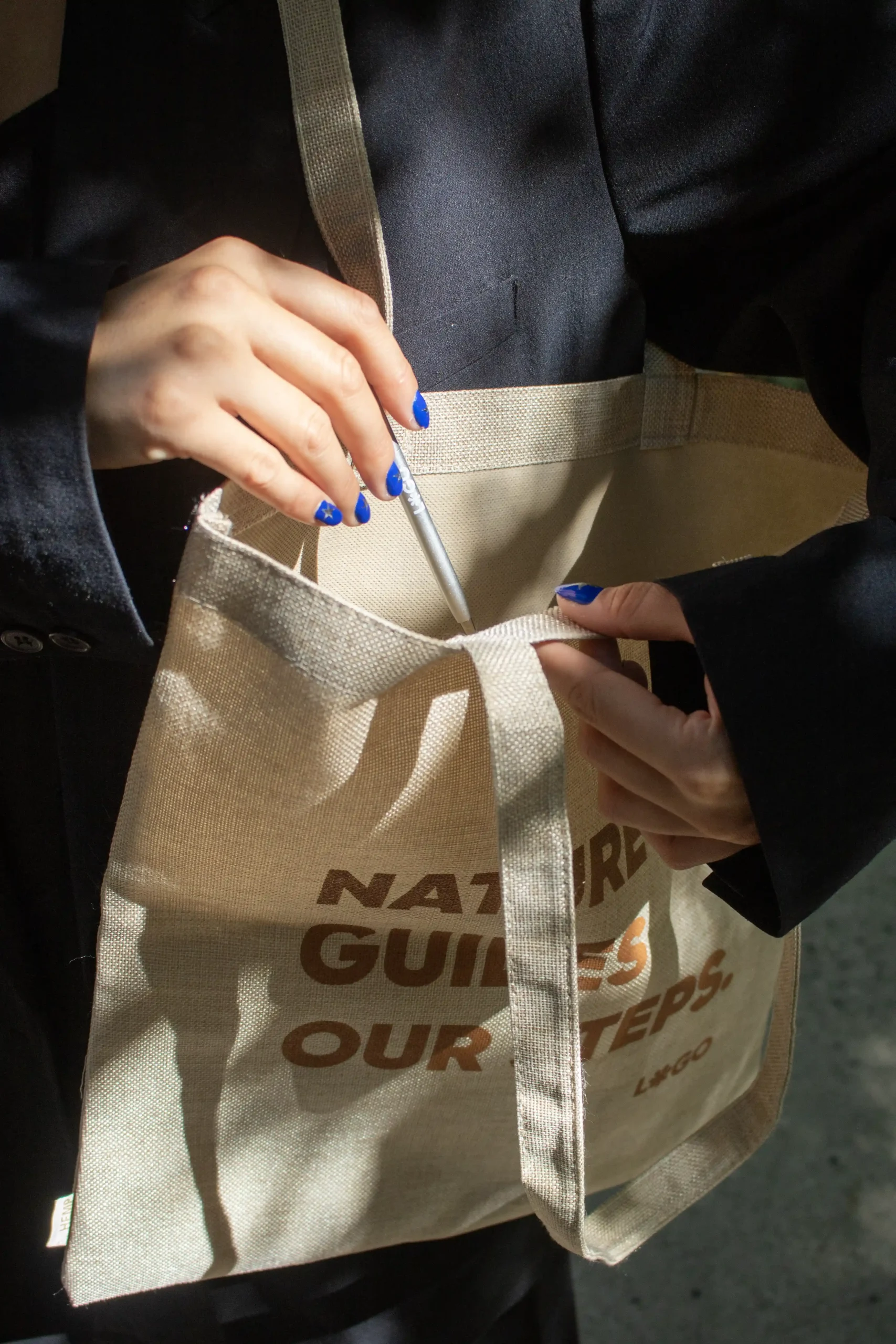 COMBO HEBRA + Bolígrafo aluminio reciclado ALI Manos introduciendo un bolígrafo de aluminio en una tote bag