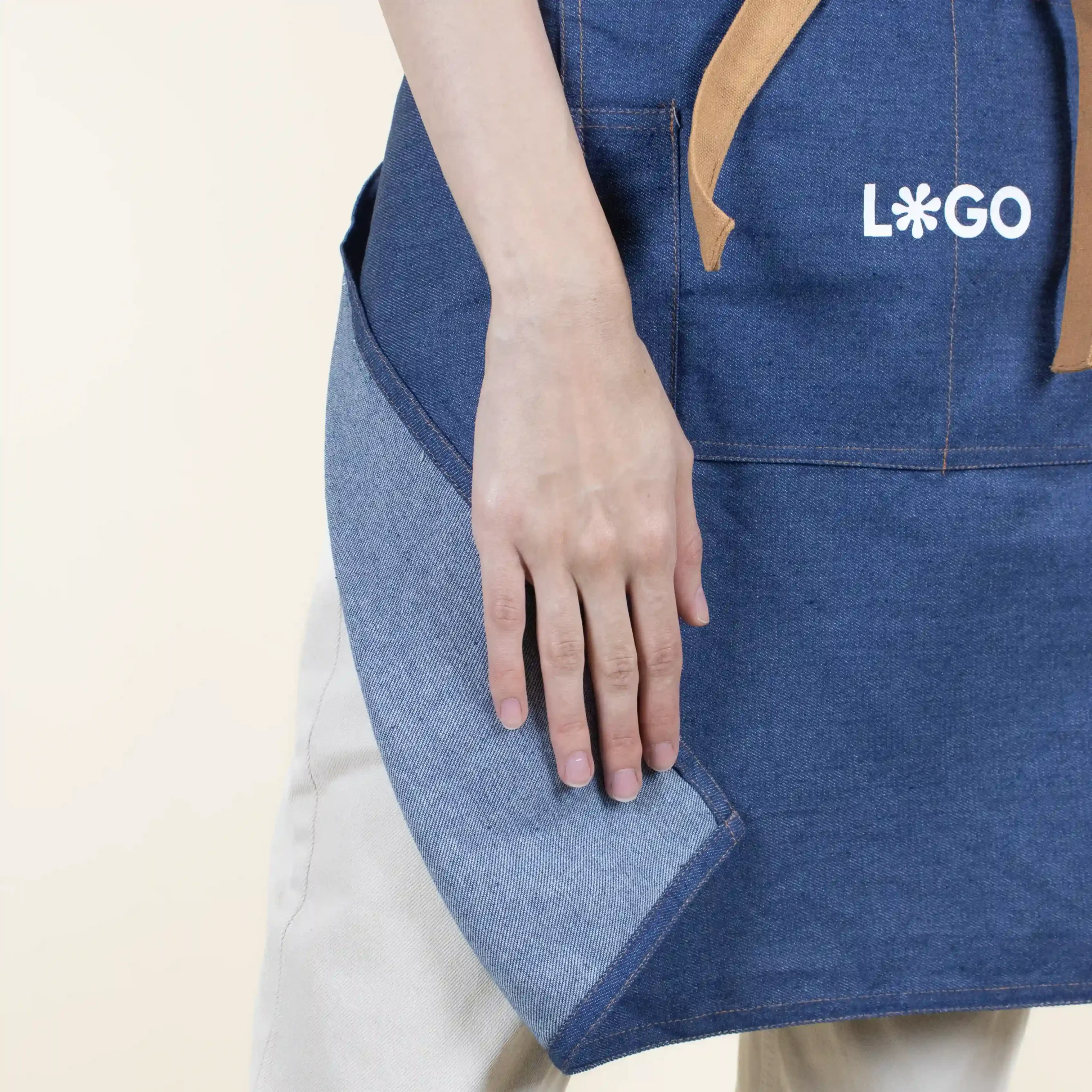 Tablier en jean personnalisé avec logo blanc, modèle fille, détail main, fond beige