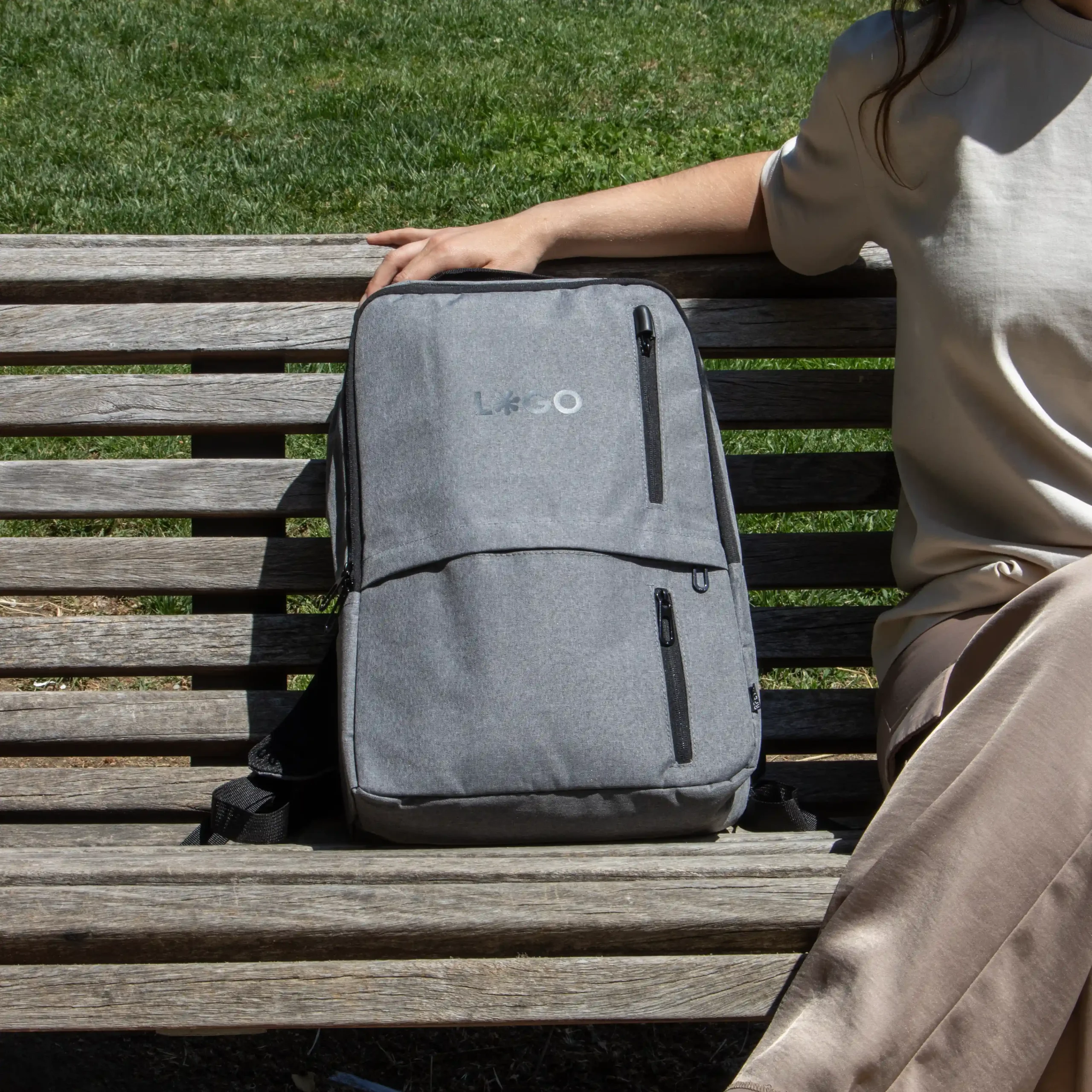 Mochila de empresa personalizada gris con logo negro modelo chica sentada en banco parque