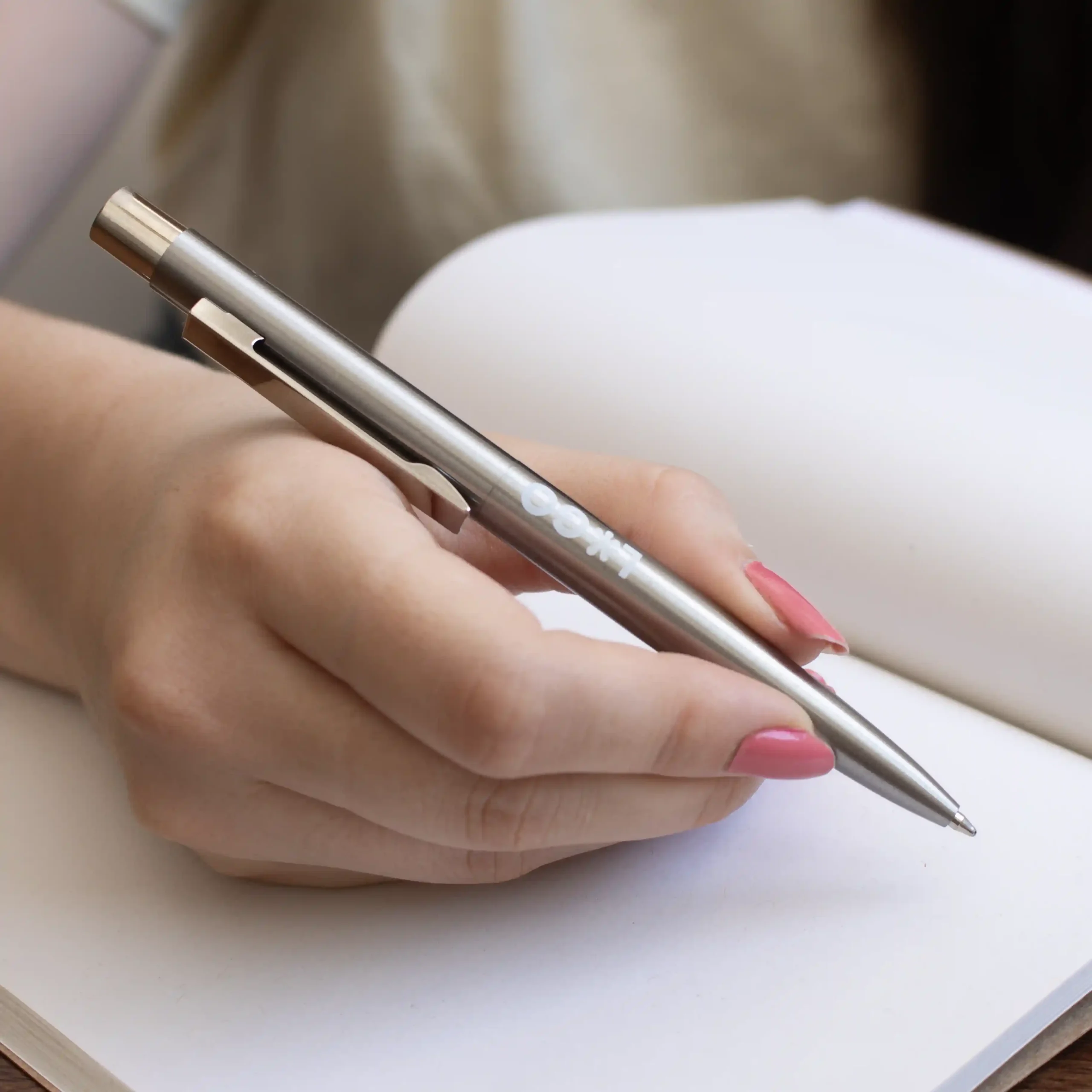 A hand jotting down notes in a notebook using a custom stainless steel pen