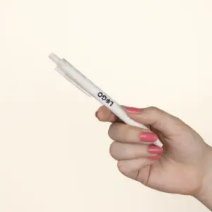 Mano sujetando bolígrafo de caña de trigo blanco personalizado con logo sobre fondo beige