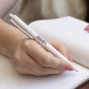 Mano escribiendo en cuaderno con bolígrafo de caña de trigo blanco personalizado con logo