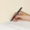 Mano escribiendo en cuaderno con bolígrafo de fibra de cafe personalizado con logo blanco