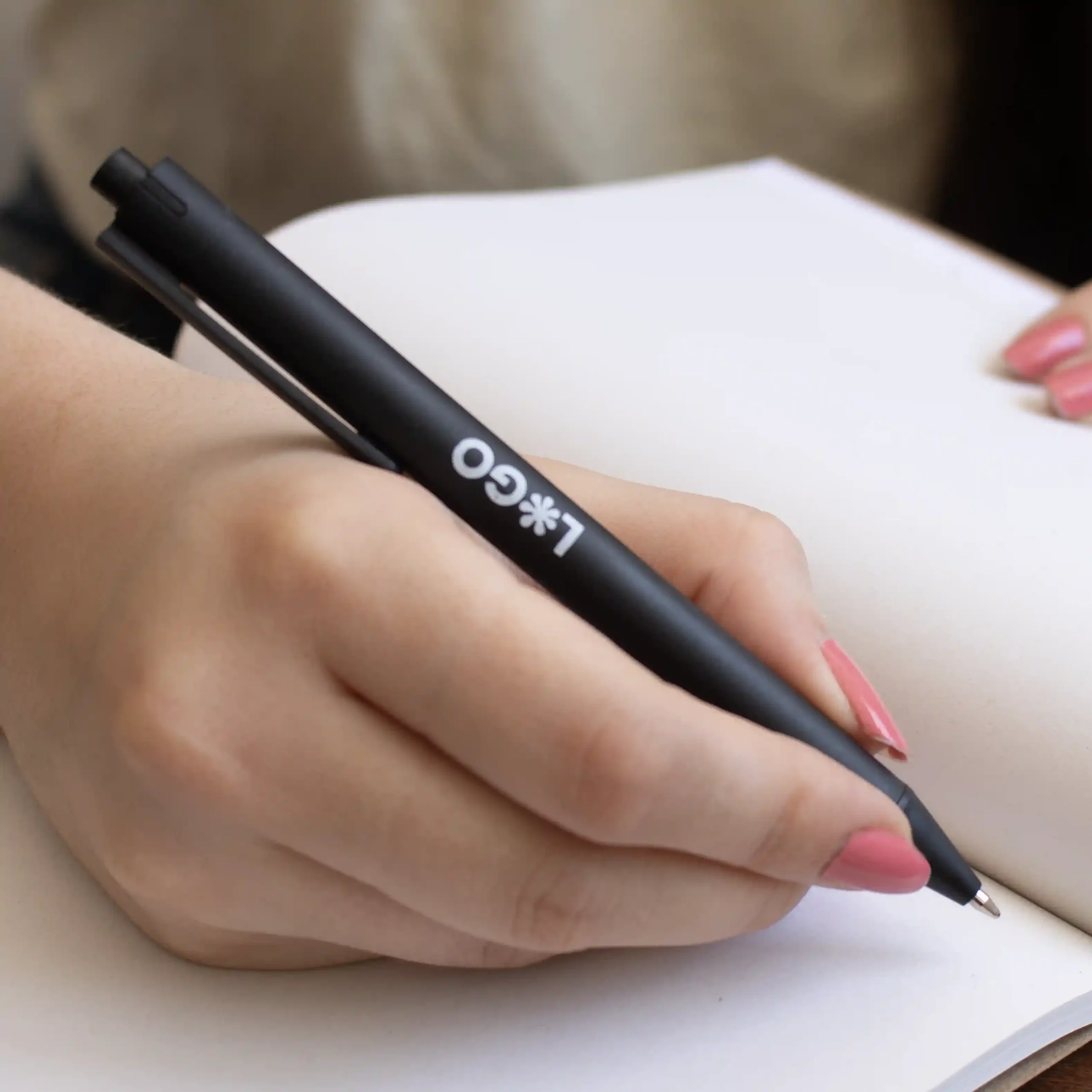 A hand jotting down in a notebook using a custom black wheat pen
