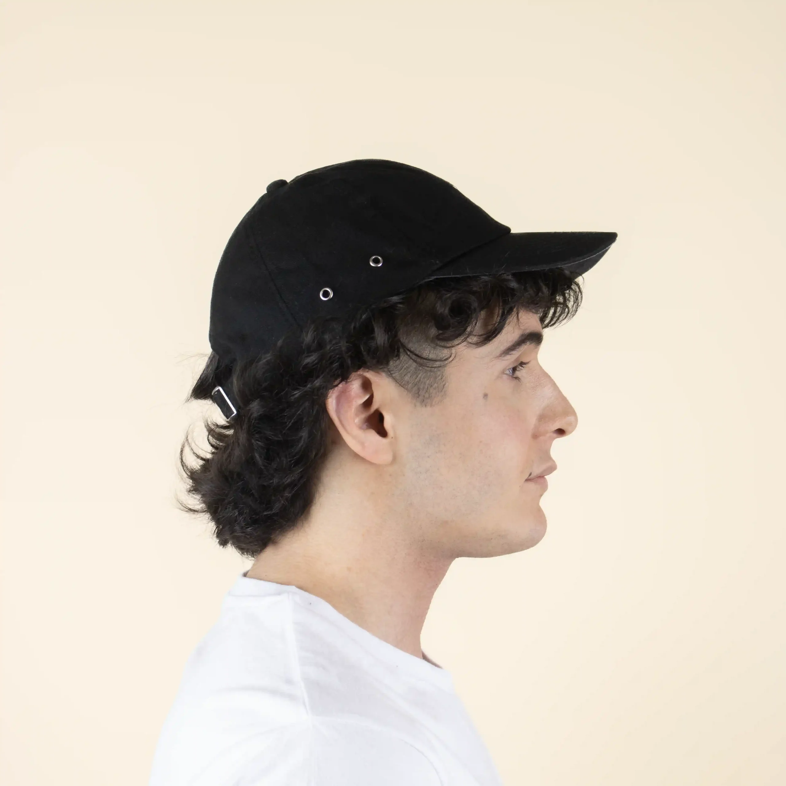 Casquette noire personnalisée modèle homme en position latérale sur fond beige.