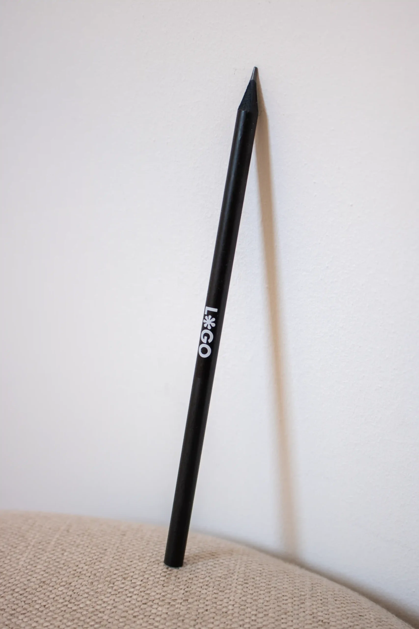 Crayon écologique en bois noir personnalisé avec logo blanc appuyé contre un mur