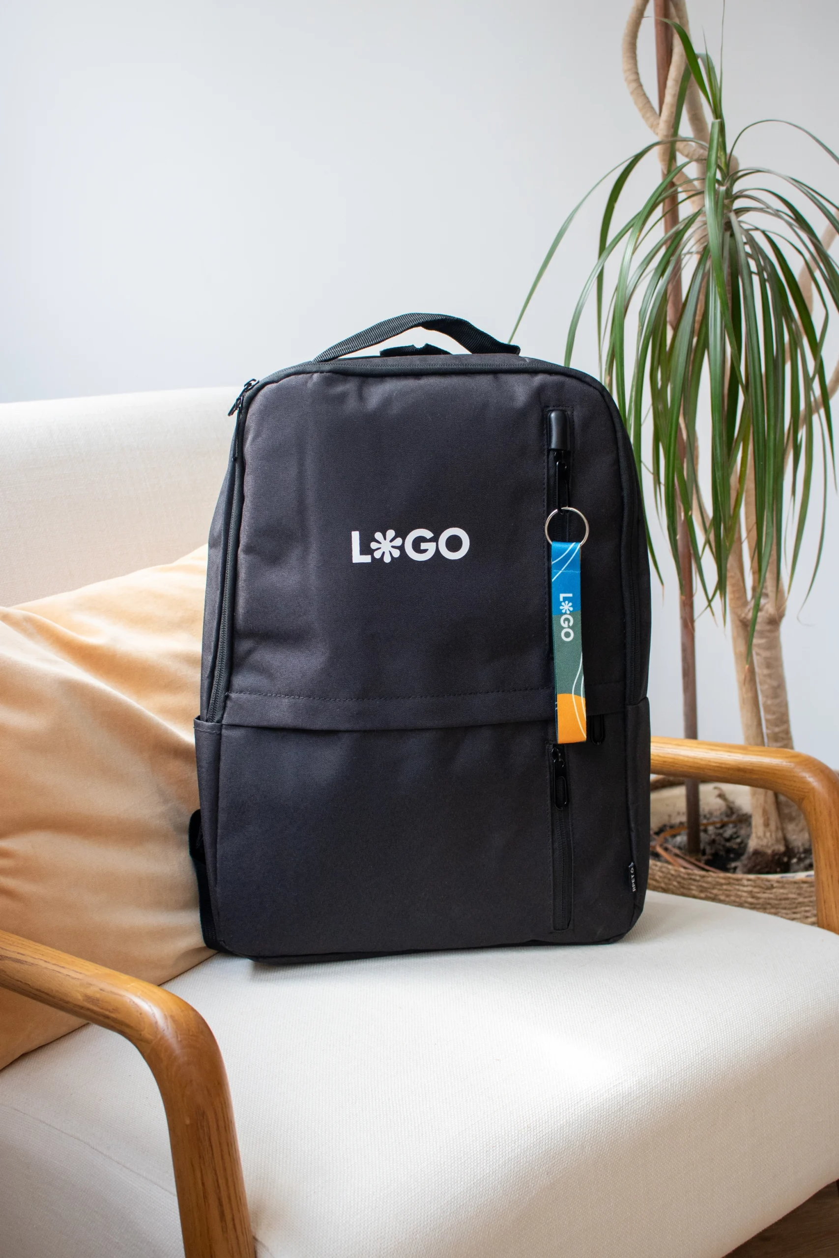 Mochila DUPPIA + Llavero ecológico CLAUS Mochila negra con un llavero ecológico personalizado con logo sobre un sillón