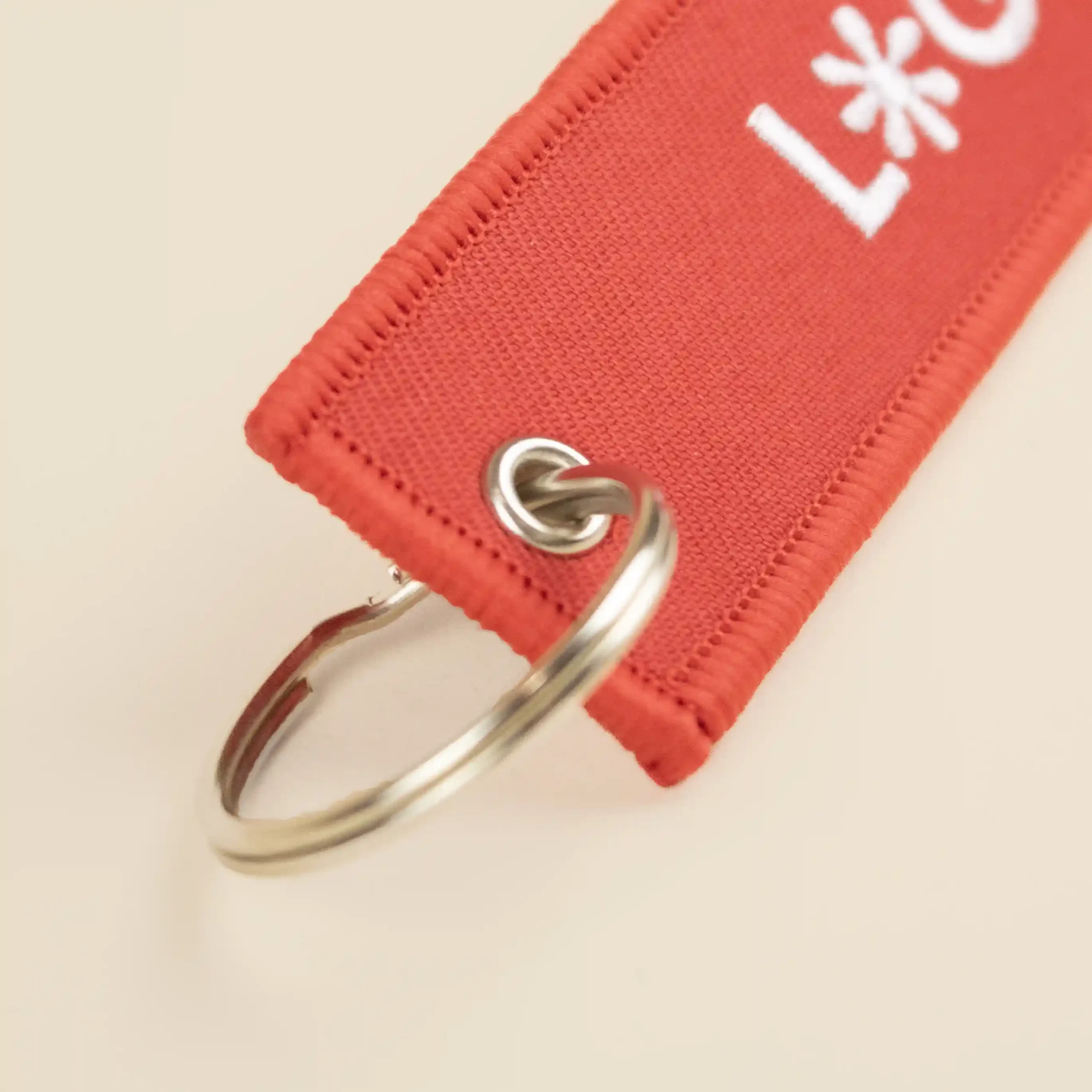 Llavero de tela bordado FILOS Detalle Anilla metálica de un llavero de tela rojo bordado con logo blanco