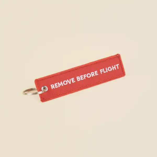 Llavero de tela rojo personalizado bordado con hilo blanco sobre fondo beige