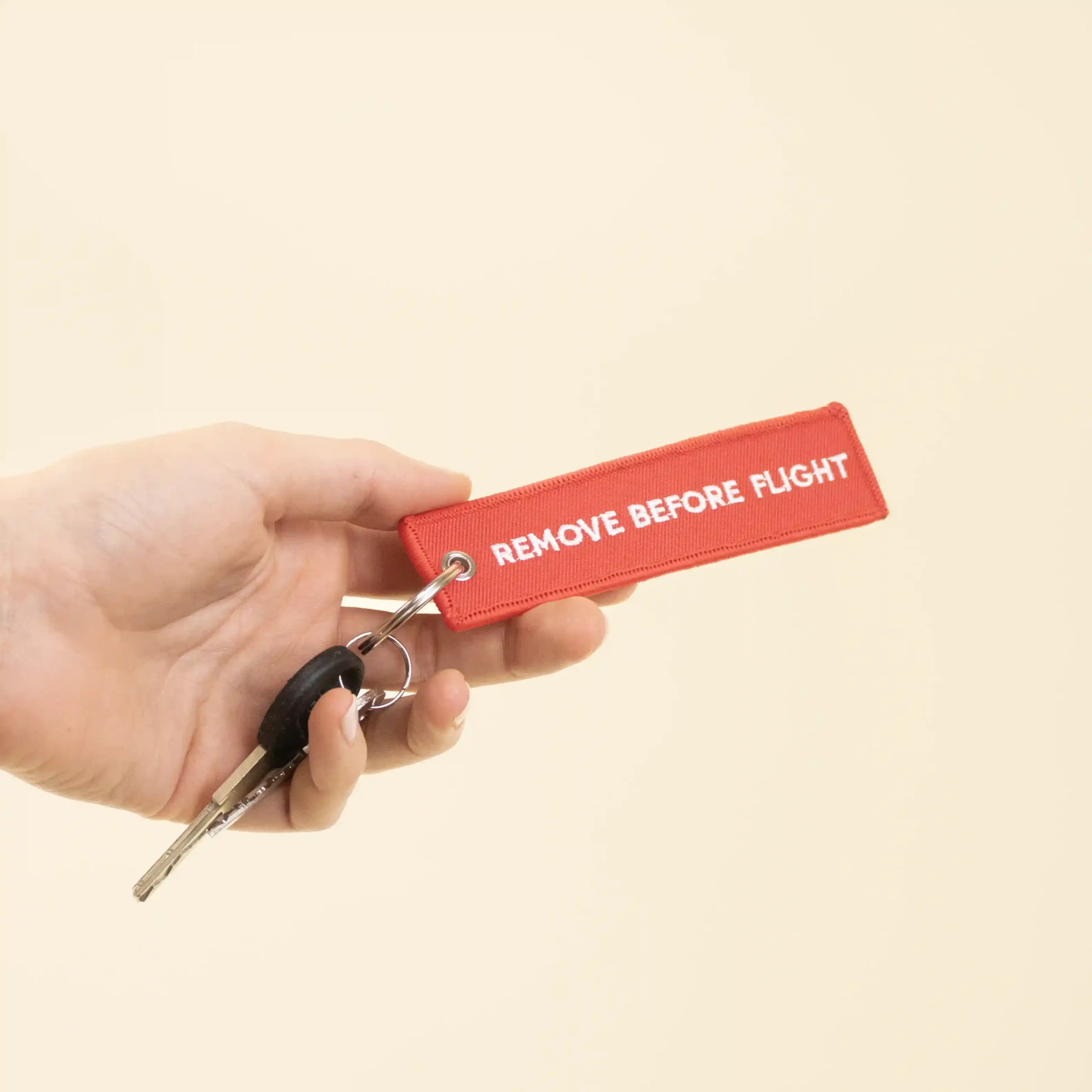 Llavero de tela bordado FILOS Llave Mano sujetando unas llaves con llavero de tela rojo personalizado bordado con hilo blanco sobre fondo beige