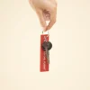 Mano sujetando unas llaves con llavero de tela rojo bordado con hilo blanco sobre fondo beige