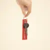 Mano sujetando unas llaves con llavero de tela rojo bordado con hilo blanco sobre fondo beige