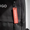 Llavero de tela rojo personalizado bordado con hilo blanco colgado de la cremallera de una mochila negra