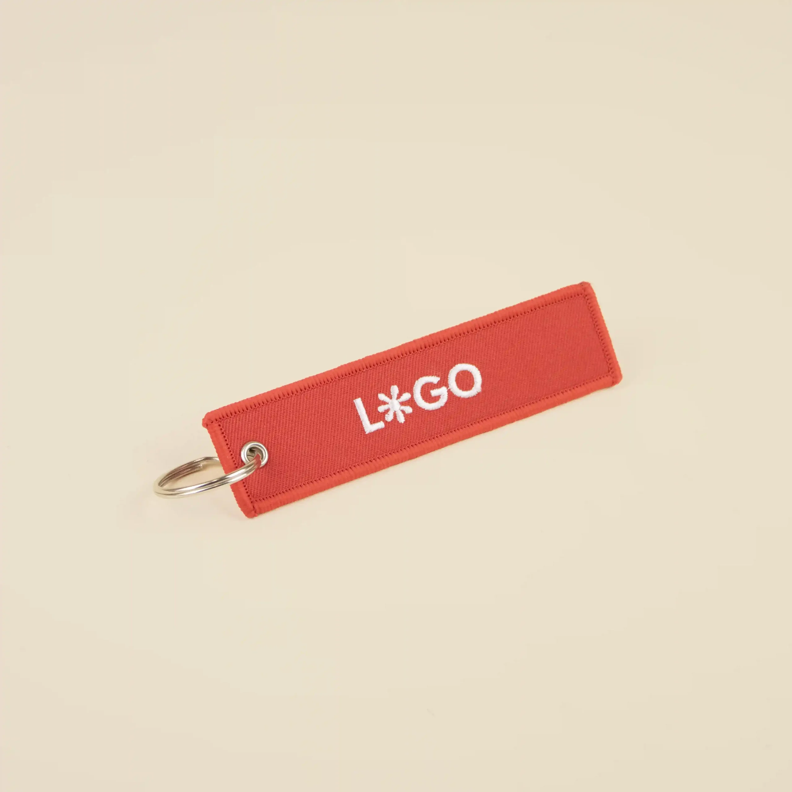 Llavero de tela bordado FILOS Llavero de tela rojo personalizado bordado con hilo blanco sobre fondo beige