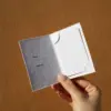Mano mostrando un porta llaves de hotel díptico en papel ecológico blanco abierto con una tarjeta blanca dentro