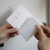 Mano delante de una puerta de hotel mostrando un porta llaves de hotel en papel ecológico blanco abierto con una tarjeta blanca dentro
