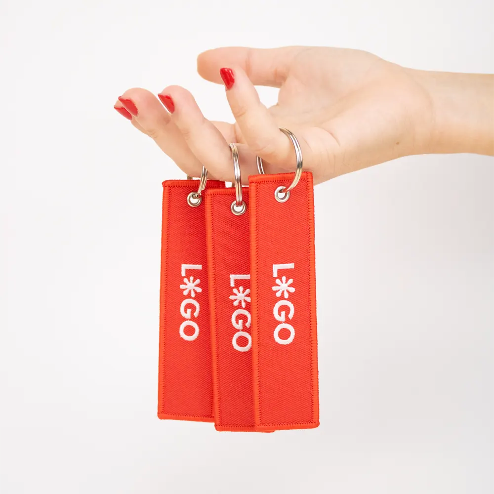 Keyring FILOS Mano sujetando 3 llaveros de tela rojos personalizados con logo blanco