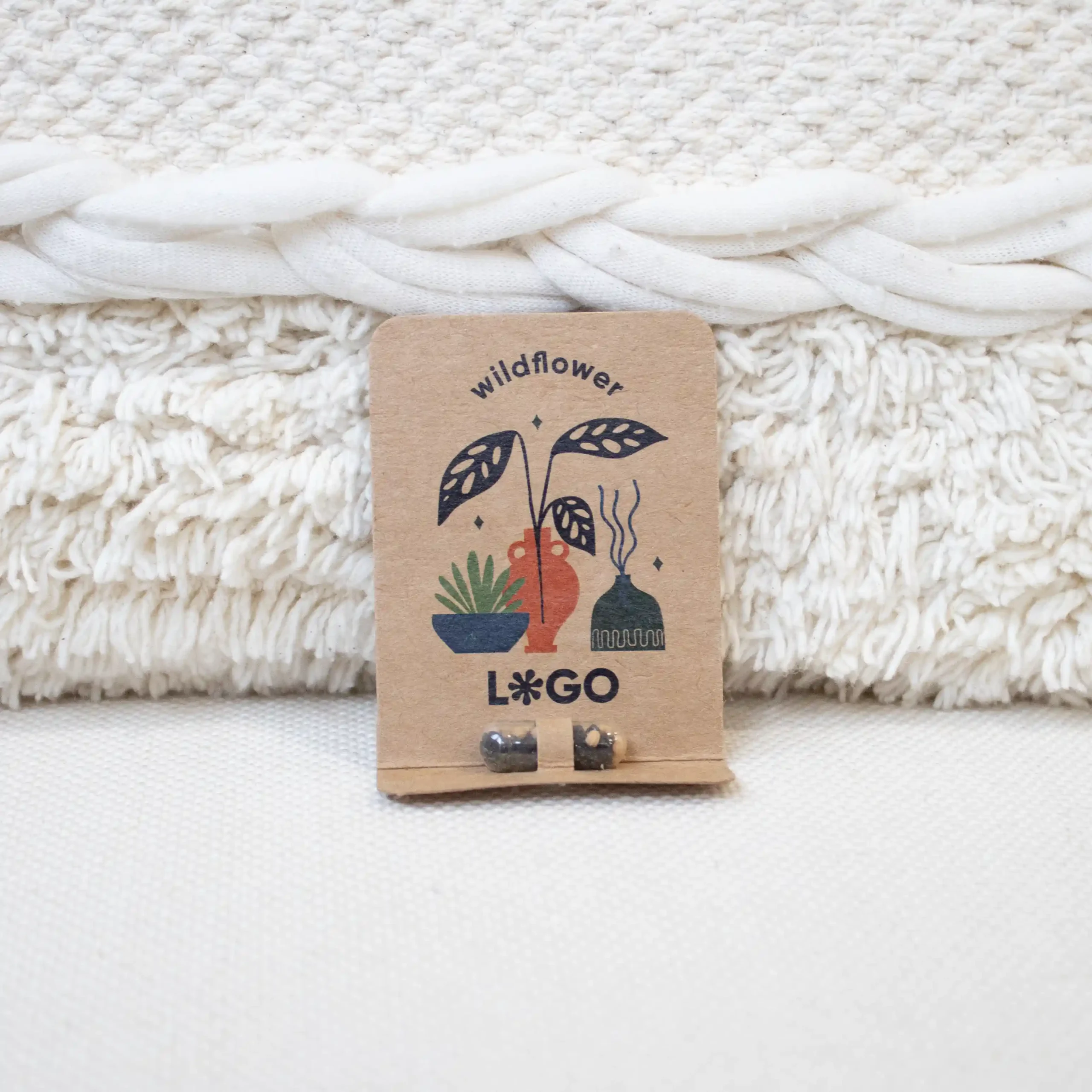 Earth Pill Cápsula de semillas EMMA KRAFT Cápsula biodegradable con semillas en su interior con packaging de cartón kraft personalizado apoyada en un cojín blanco