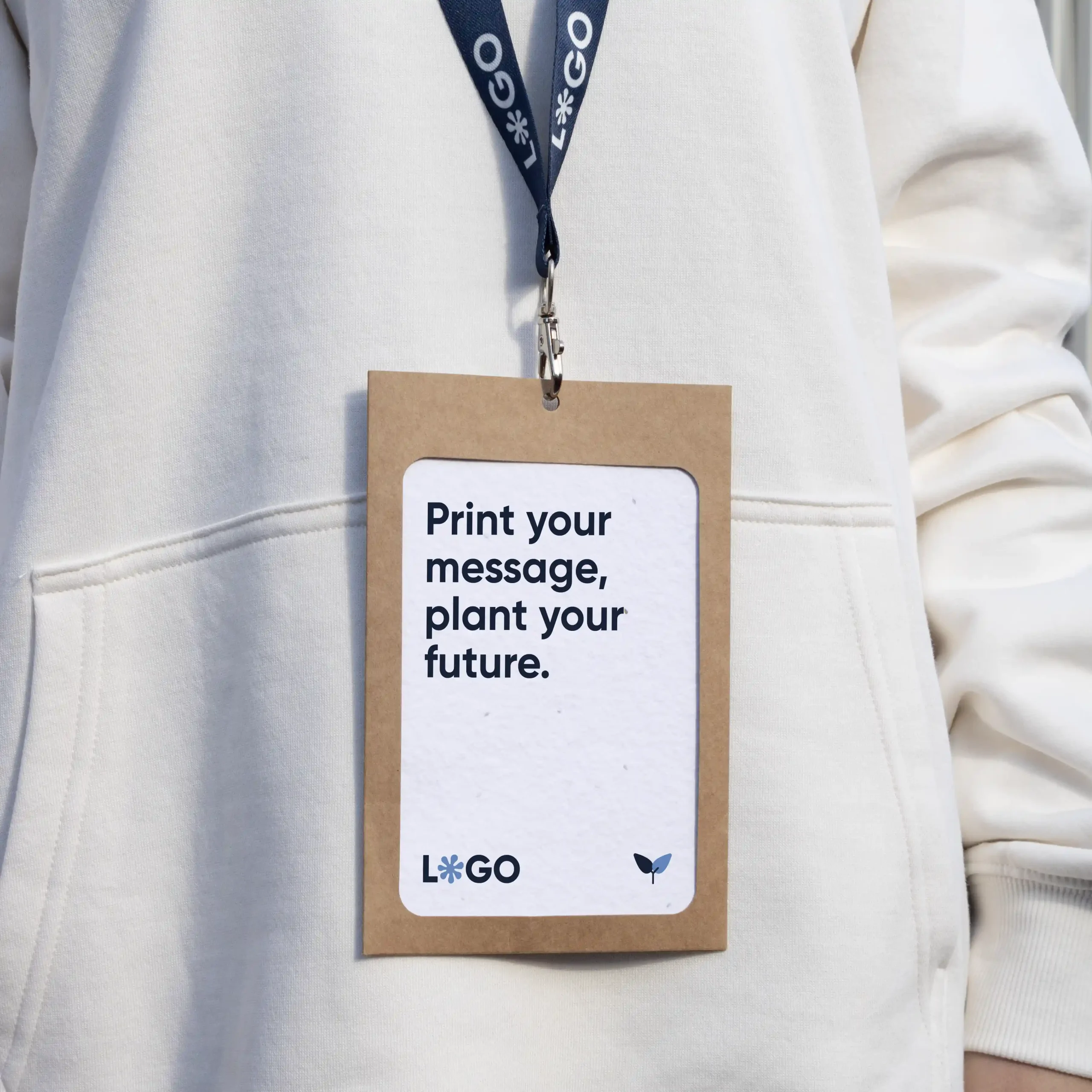 Kit C: Acreditación plantable, Funda KASE 0/0 y Lanyard COLLIN Acreditación personalizada con funda kraft y lanyard de rPET azul personalizado con el texto 'logo' en blanco colgado del cuello de una persona con jersey blanco