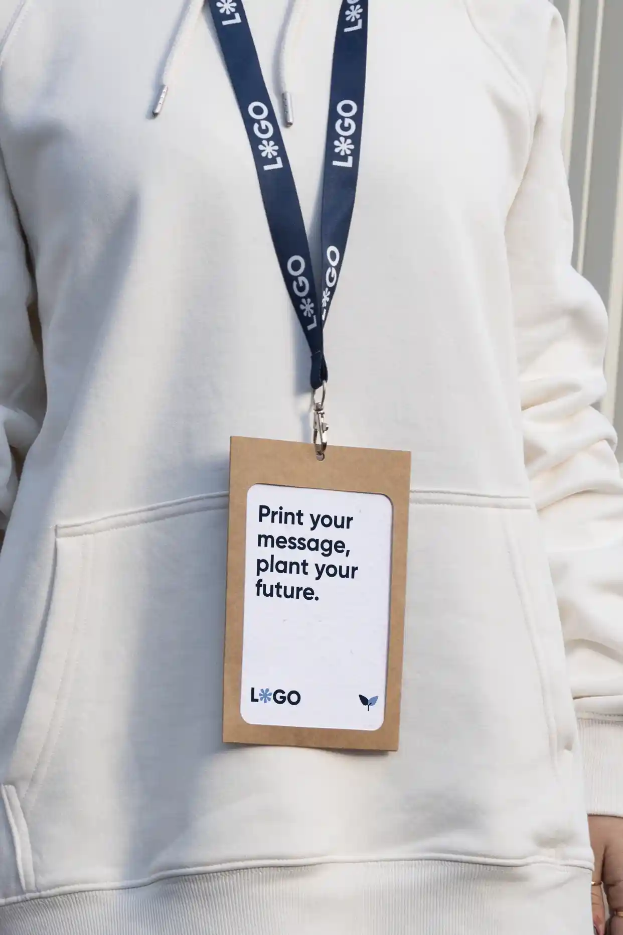 Acreditación eco, Funda KASE 0/0 y Lanyard COLLIN Acreditación personalizada con funda kraft y lanyard de rPET azul personalizado con el texto 'logo' en blanco colgado del cuello de una persona con jersey blanco