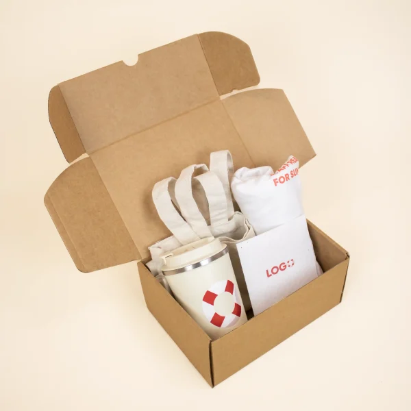 Caja de cartón abierta con una taza take away, un flyer, una camiseta blanca y una tote bag de tela