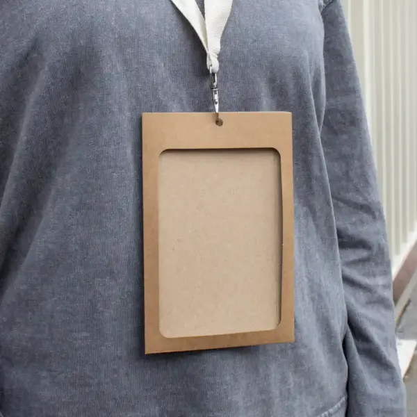 Funda de acreditación de cartón kraft marrón colgada de un lanyard de algodón blanco colocado en el cuello de una persona