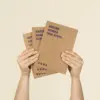 Dos manos sujetando 3 cuadernos ecológicos kraft personalizados con el texto 'Nature guides our steps'