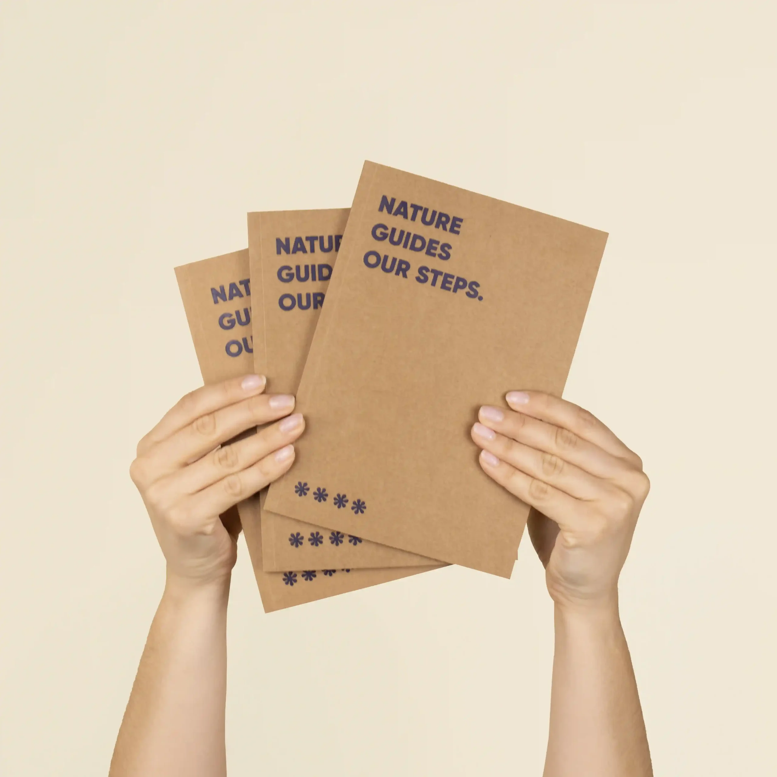 Cuaderno ecológico KLAAS 1/0 Dos manos sujetando 3 cuadernos ecológicos kraft personalizados con el texto 'Nature guides our steps'
