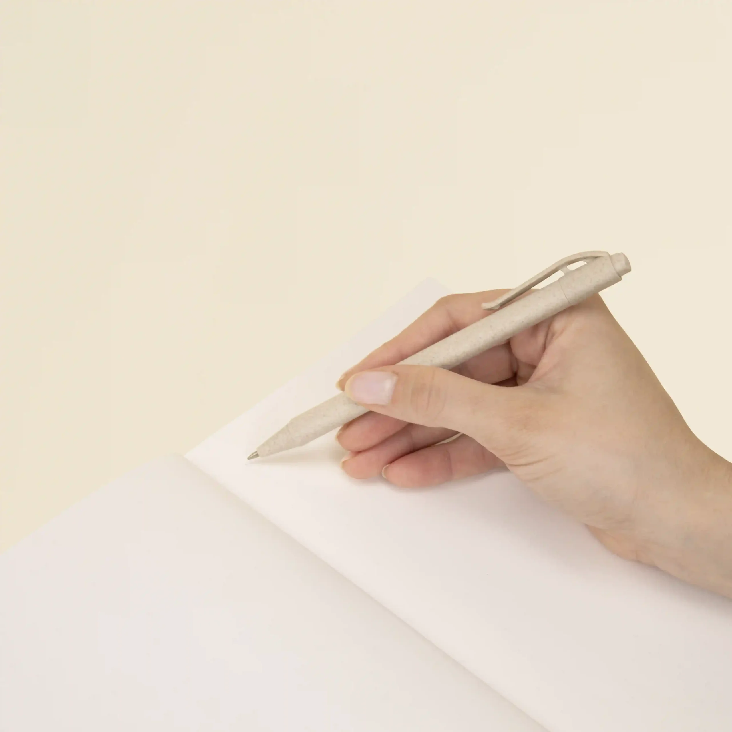 Cuaderno ecológico KLAAS 1/0 Mano sujetando un bolígrafo beige escribiendo sobre las páginas interiores de un cuaderno