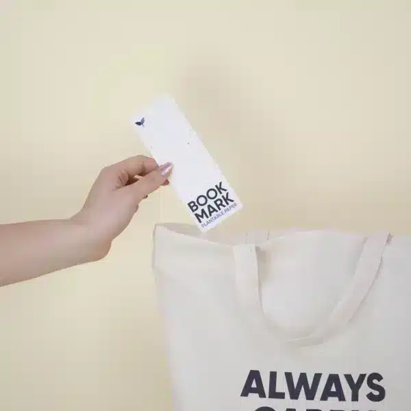 Mano metiendo un marcapáginas de papel plantable personalizado en una bolsa de algodón beige