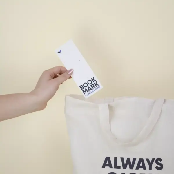 Mano metiendo un marcapáginas de papel plantable personalizado en una bolsa de algodón beige