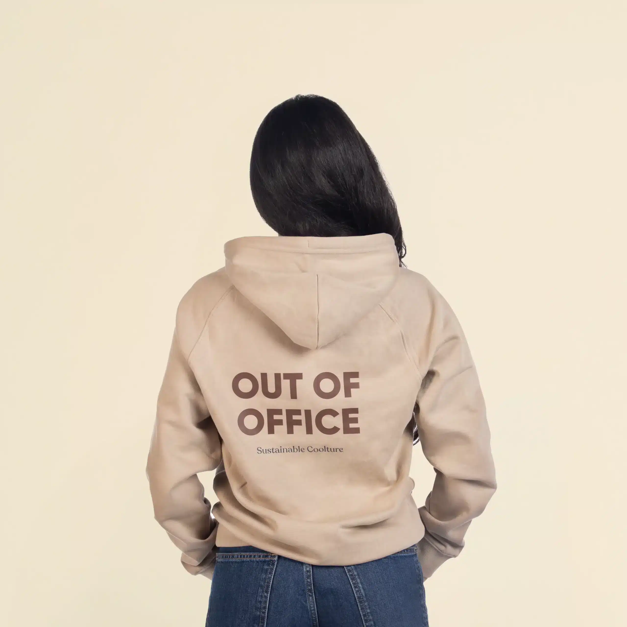 Sudadera con capucha HUVA Beige Chica morena de espaldas llevando jeans y una sudadera con capucha beige personalizada