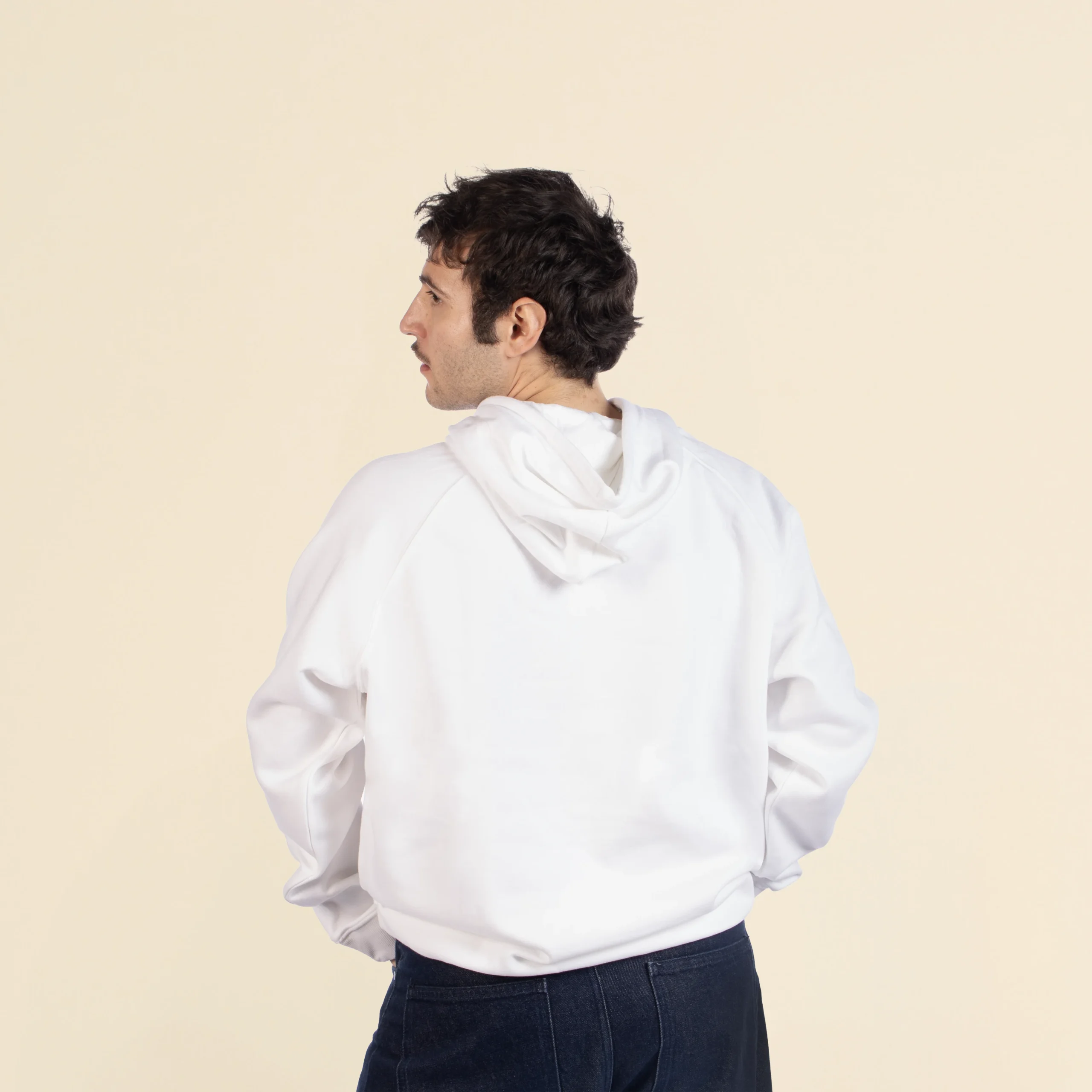 Sudadera con capucha HUVA Blanco Chico moreno de espaldas llevando jeans y una sudadera blanca con capucha personalizada