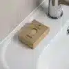 Jabón artesanal dentro una caja marrón kraft personalizada colocada sobre el mueble de un lavabo