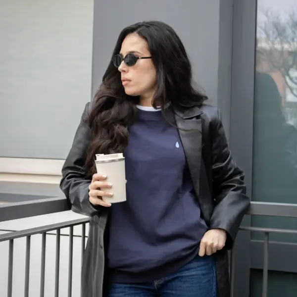 Chica morena con gafas de sol y un termo en la mano, llevando jeans y una sudadera azul personalizada