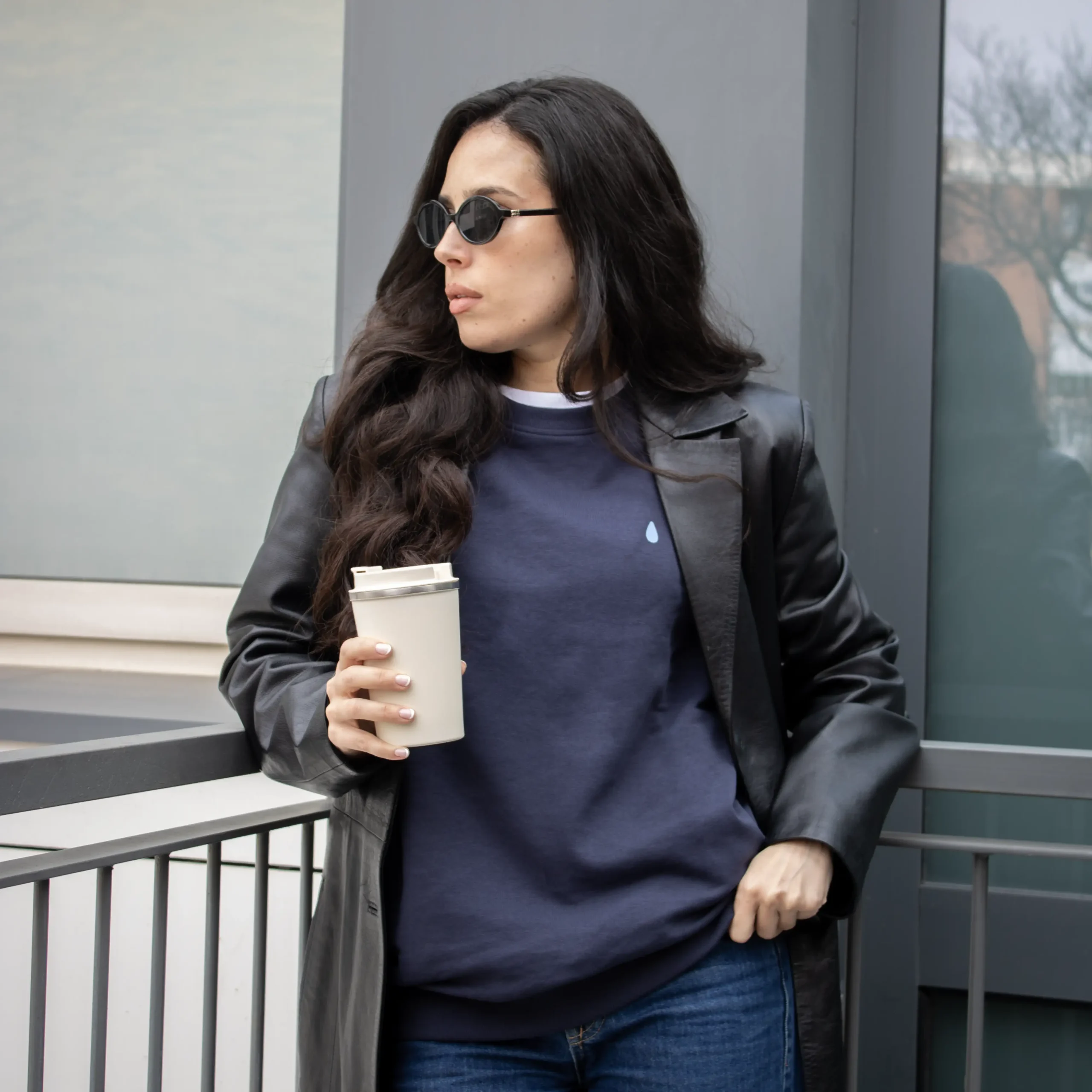 Sudadera personalizada SEDRA Azul Chica morena con gafas de sol y un termo en la mano, llevando jeans y una sudadera azul personalizada